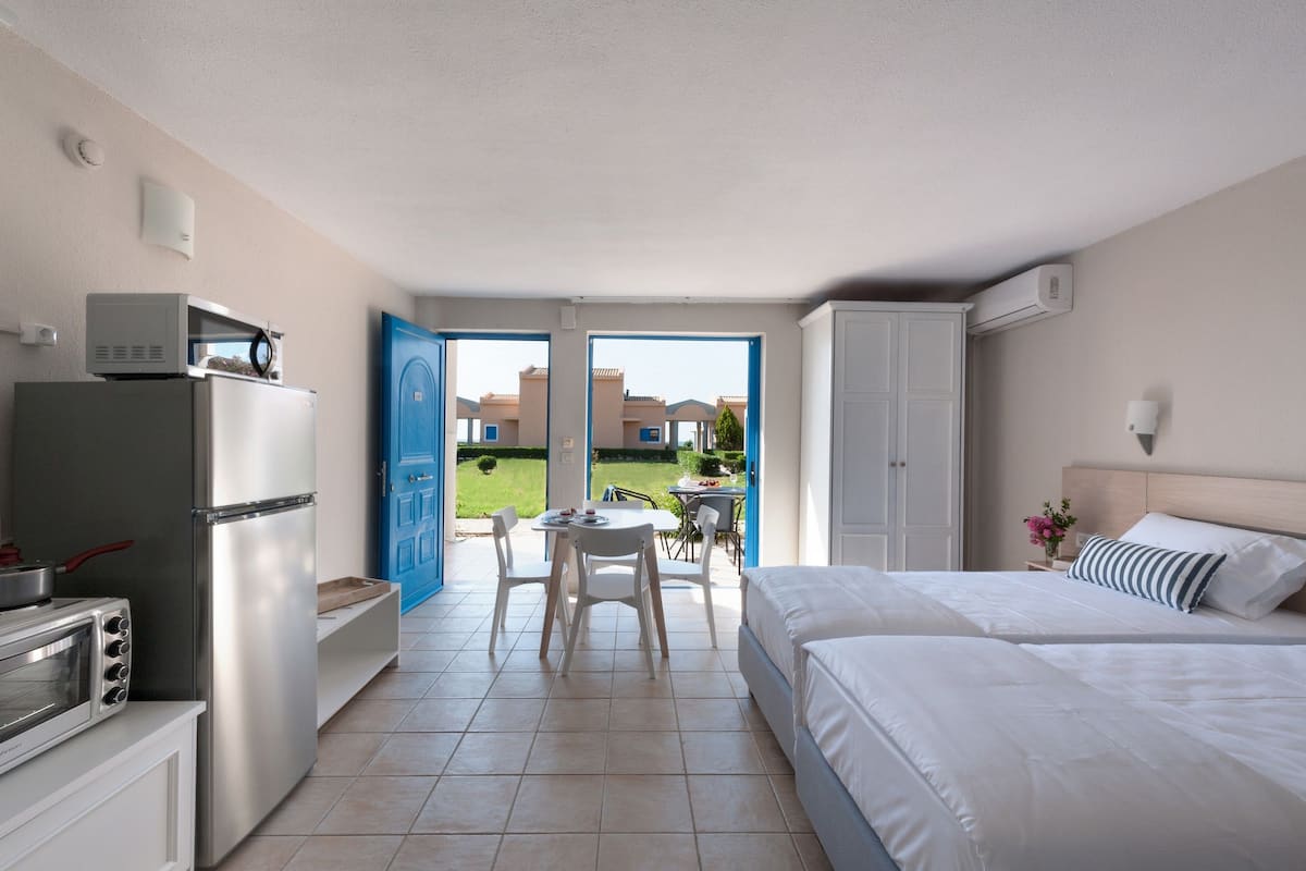 A hotel room with a kitchenette, a bed, a dining area with a table and chairs, and a view of the outside.