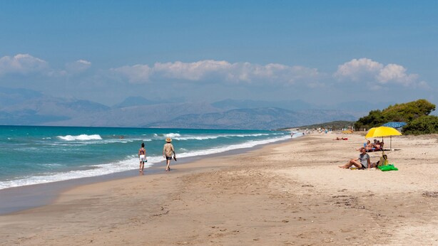 Uma praia com pessoas caminhando e sentadas sob guarda-sóis.