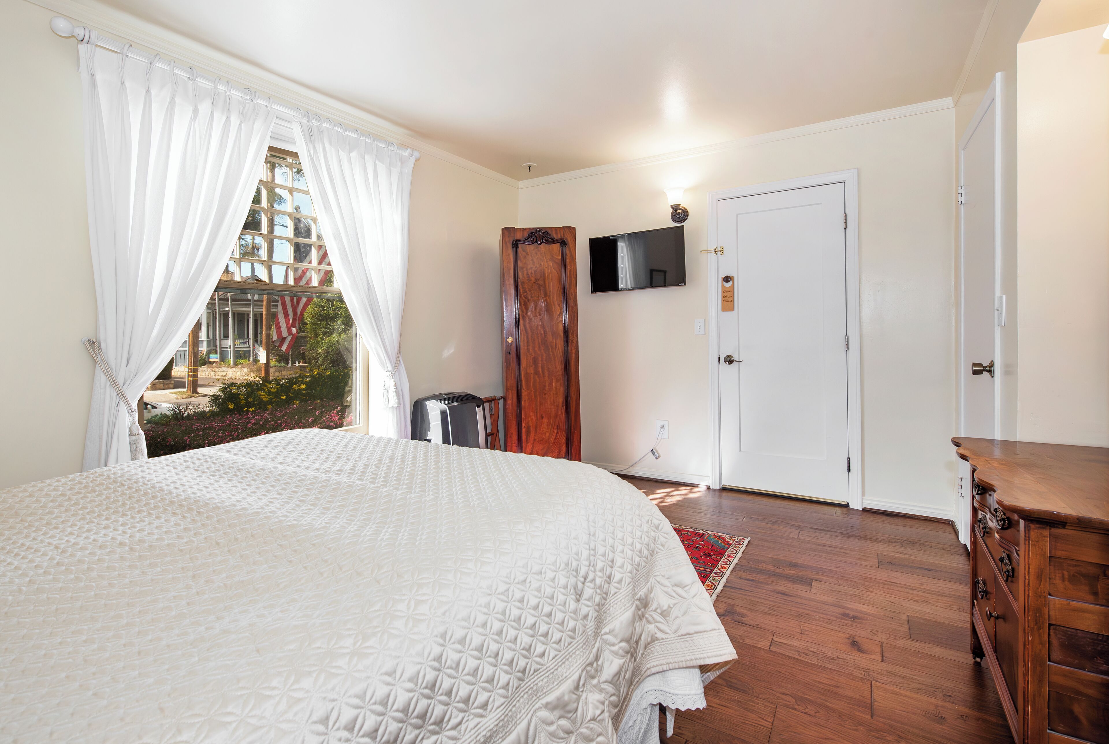 Un dormitorio con una cama grande, un aparador de madera, un televisor en la pared y una puerta.