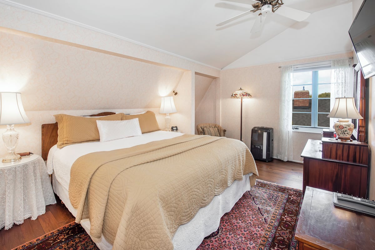 Quarto bem iluminado com uma cama grande, abajures, cômoda e janela com cortinas.
