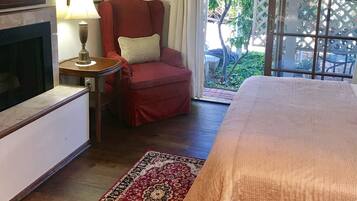 Een slaapkamer met een bed, een rode fauteuil, een open haard, een vloerkleed en uitzicht op groen.