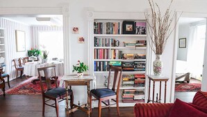 A cozy living room with a bookshelf, a dining area with a table and chairs, and a red sofa. - Bath Street Inn (Santa Barbara)