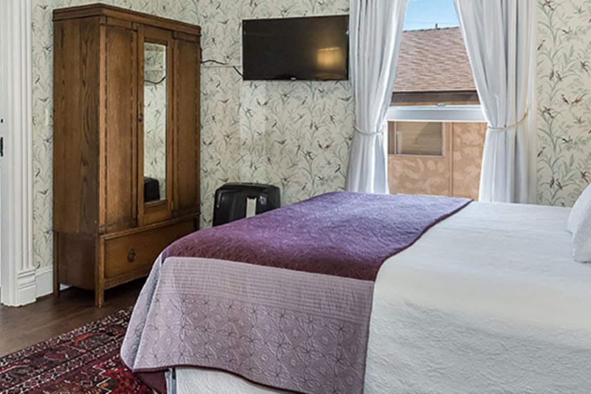Um quarto com uma cama, um guarda-roupa de madeira, uma televisão e uma janela com cortinas.