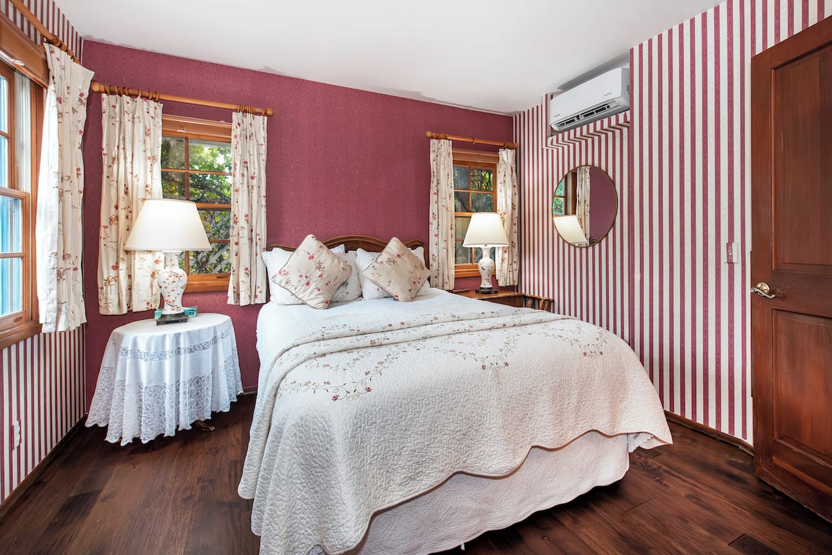 Quarto com cama grande, duas mesas de cabeceira com luminárias, um espelho redondo e papel de parede listrado.