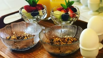 Una bandeja de desayuno con fruteros, un vaso de jugo de naranja y un tazón de granola.