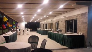 A banquet hall with round tables covered in green tablecloths, chairs with white covers, and a stage at the front. - Park Palace Hotel (Kolkata)