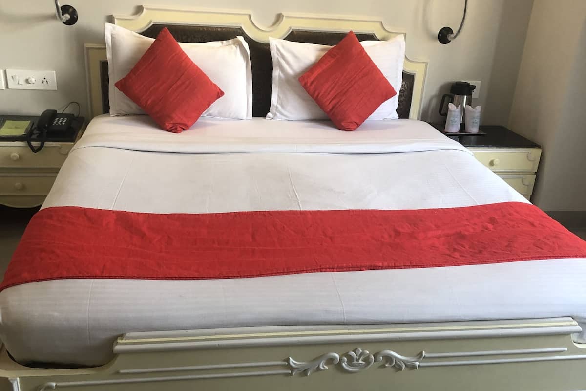 Una cama con colcha blanca y roja, dos almohadas rojas y cabecero blanco.