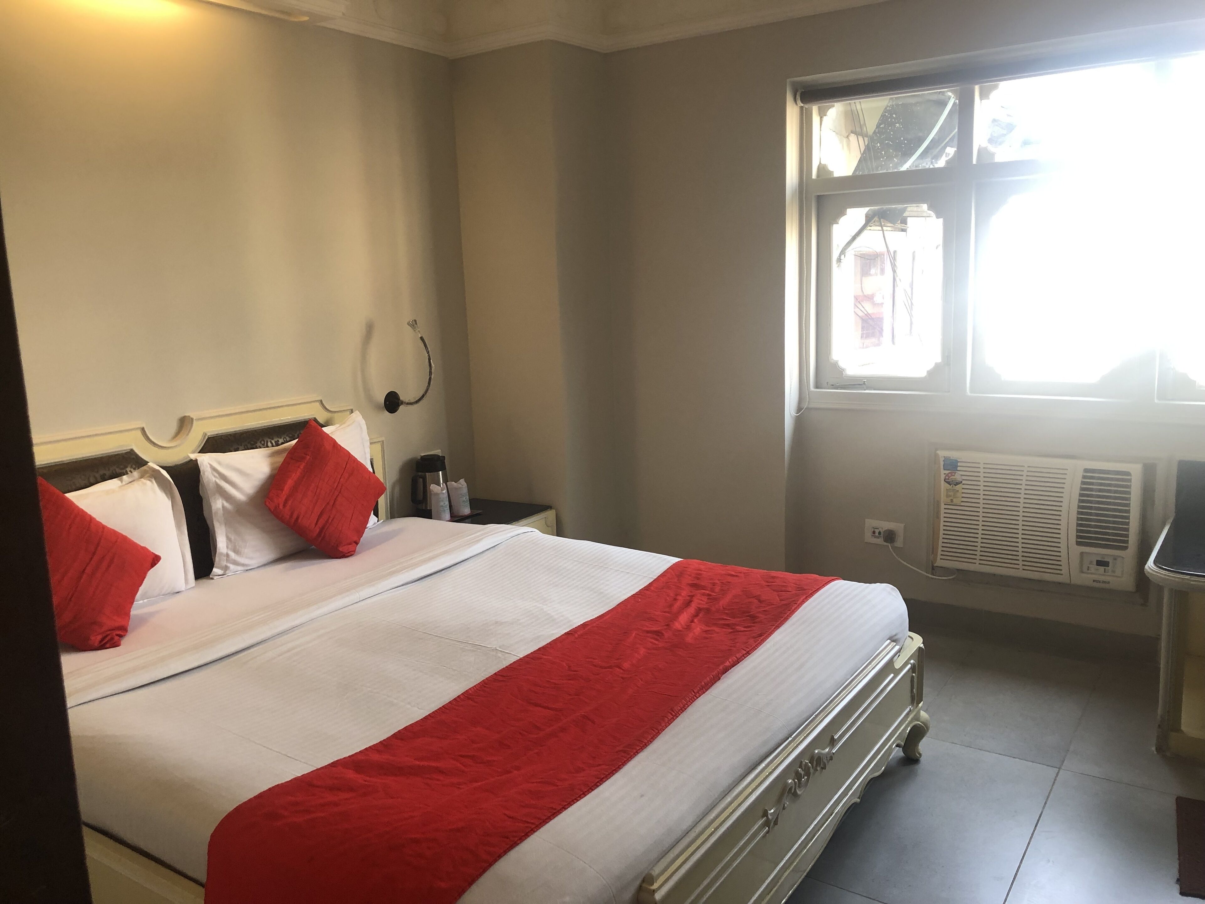 A hotel room with a bed, a nightstand, a window, and an air conditioning unit.