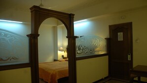 A room with a bed, a nightstand, a lamp, and a door with a sign. - Park Palace Hotel (Kolkata)