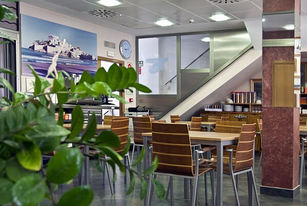 A modern library with wooden tables and chairs, a large clock on the wall, and a staircase leading to an upper level.