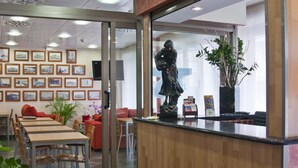 A reception area with a wooden counter, framed pictures on the wall, a statue, and a potted plant. - Hotel Marina Peñíscola (Peniscola)