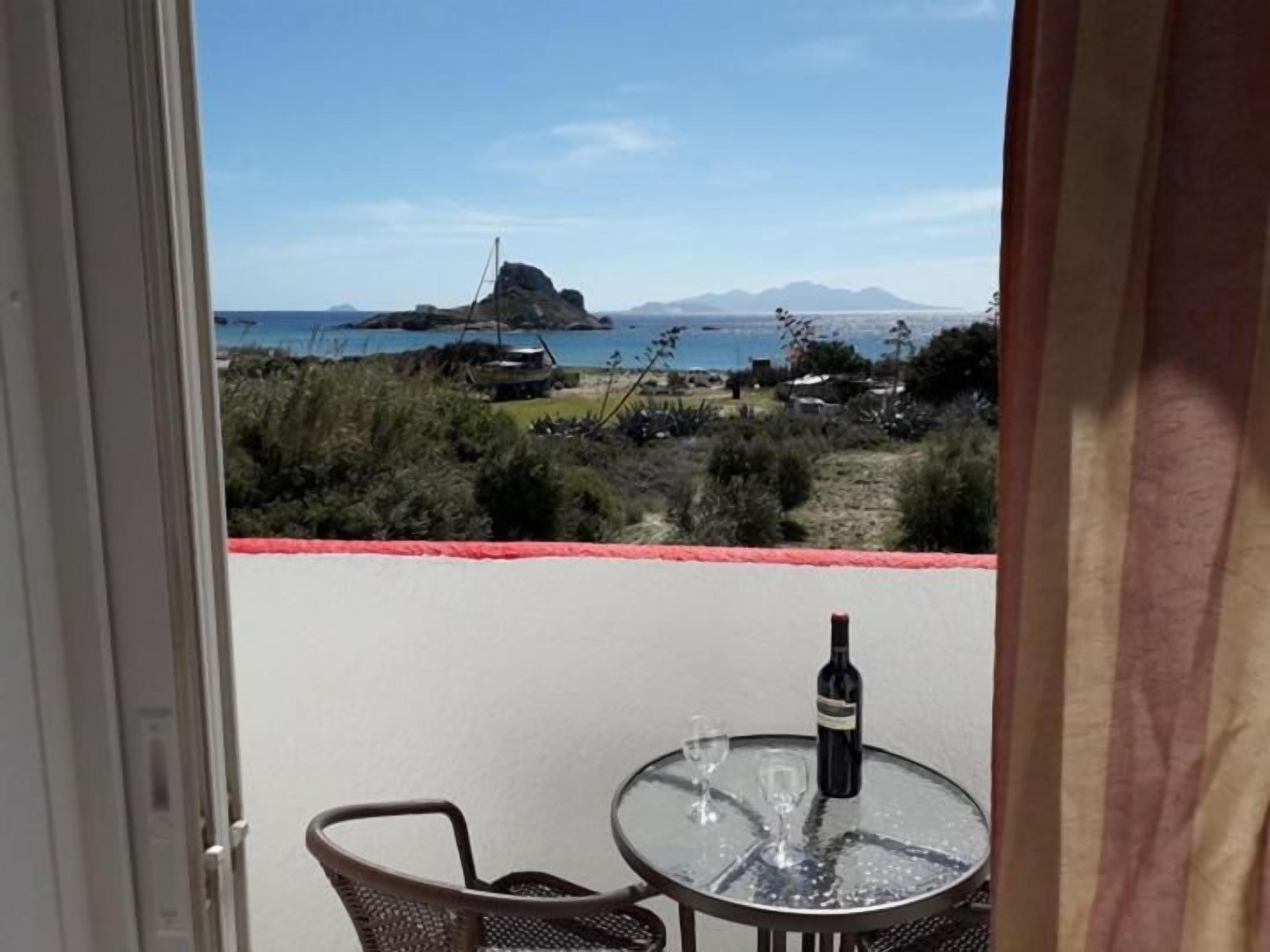 A balcony with a table and chairs, a bottle of wine, and a view of the sea and mountains.
