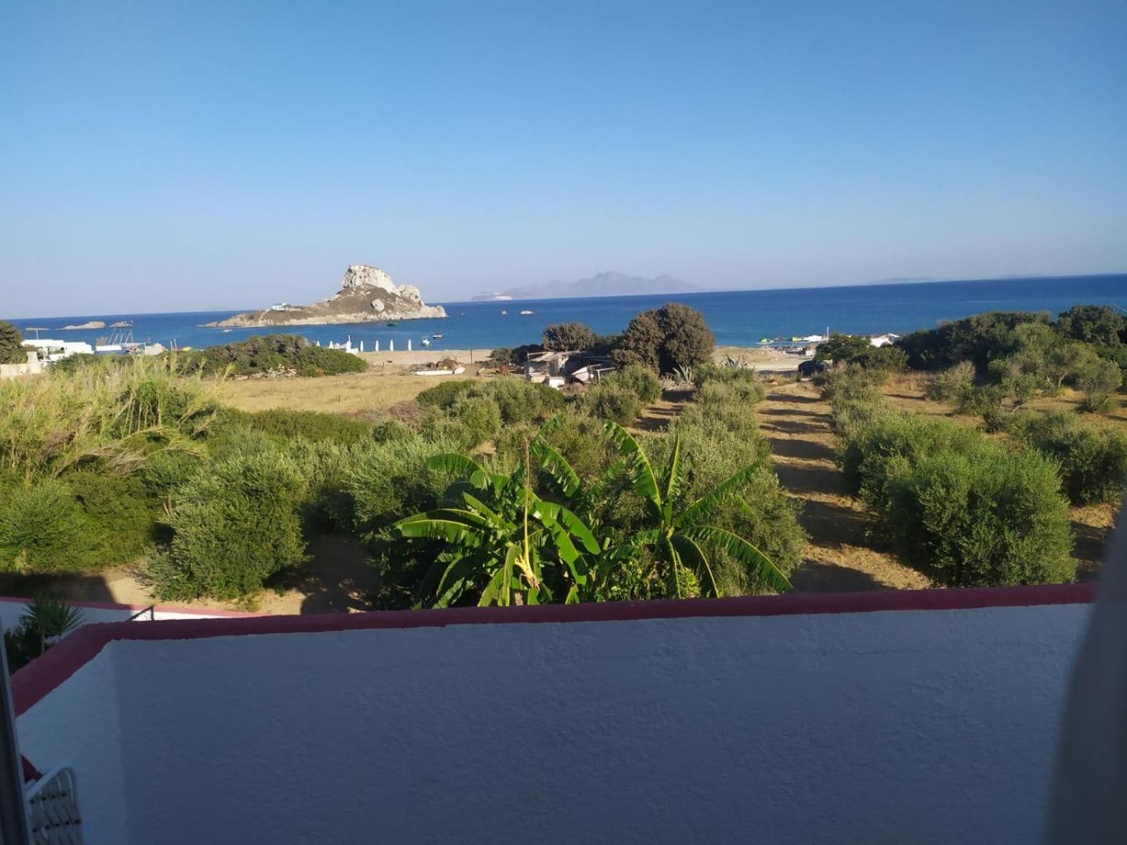 Paesaggio costiero con vista sul mare, uno sperone roccioso e un sentiero che si inoltra nella vegetazione.