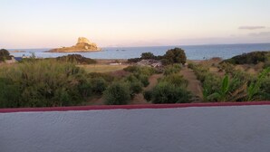 Un paisaje costero con una formación rocosa destacada, un sendero que lleva a una playa y vegetación escasa.