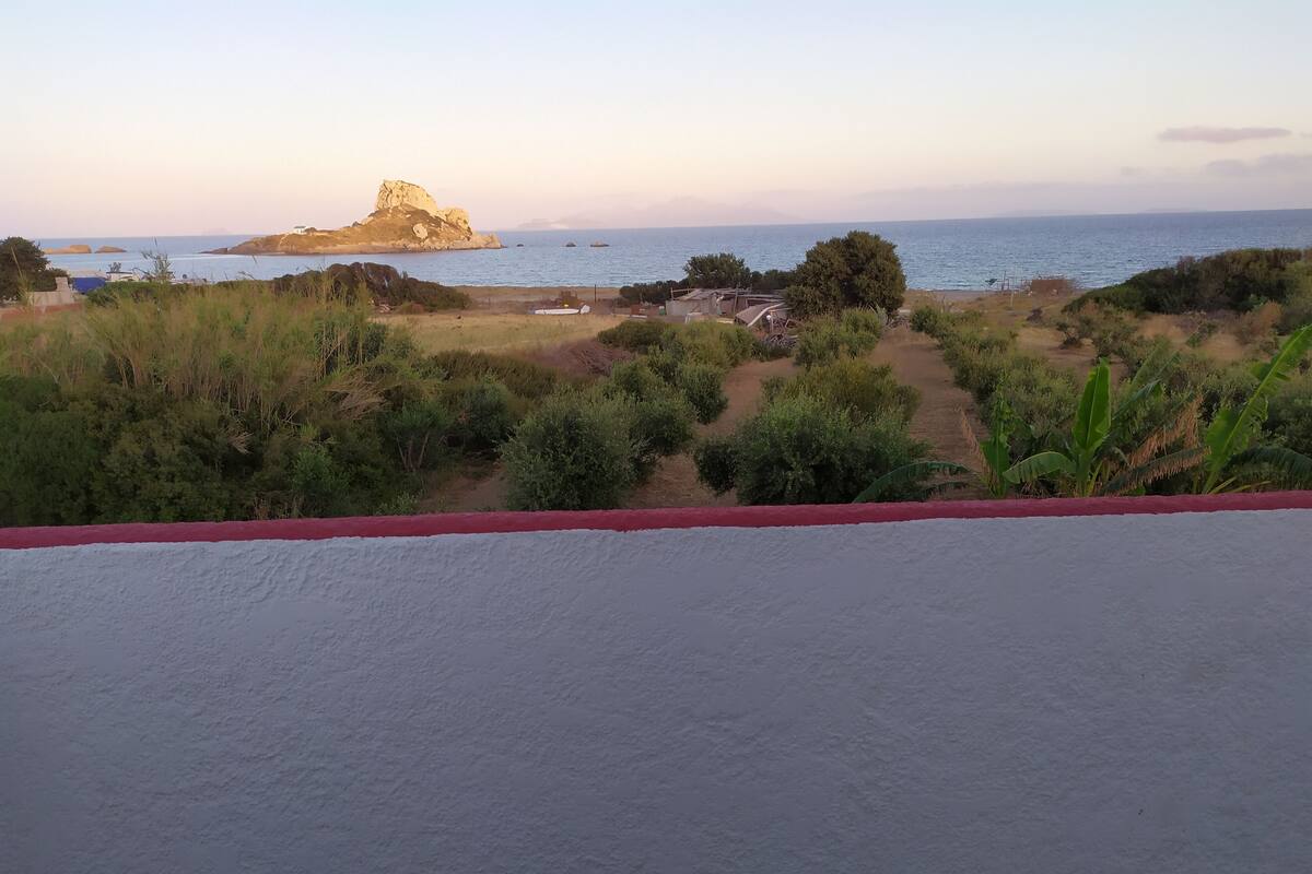 A coastal landscape with a prominent rock formation, a path leading to a beach, and sparse vegetation.