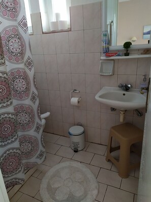 A bathroom with a toilet, sink, and shower curtain. - Kaluva Studios (Kos)