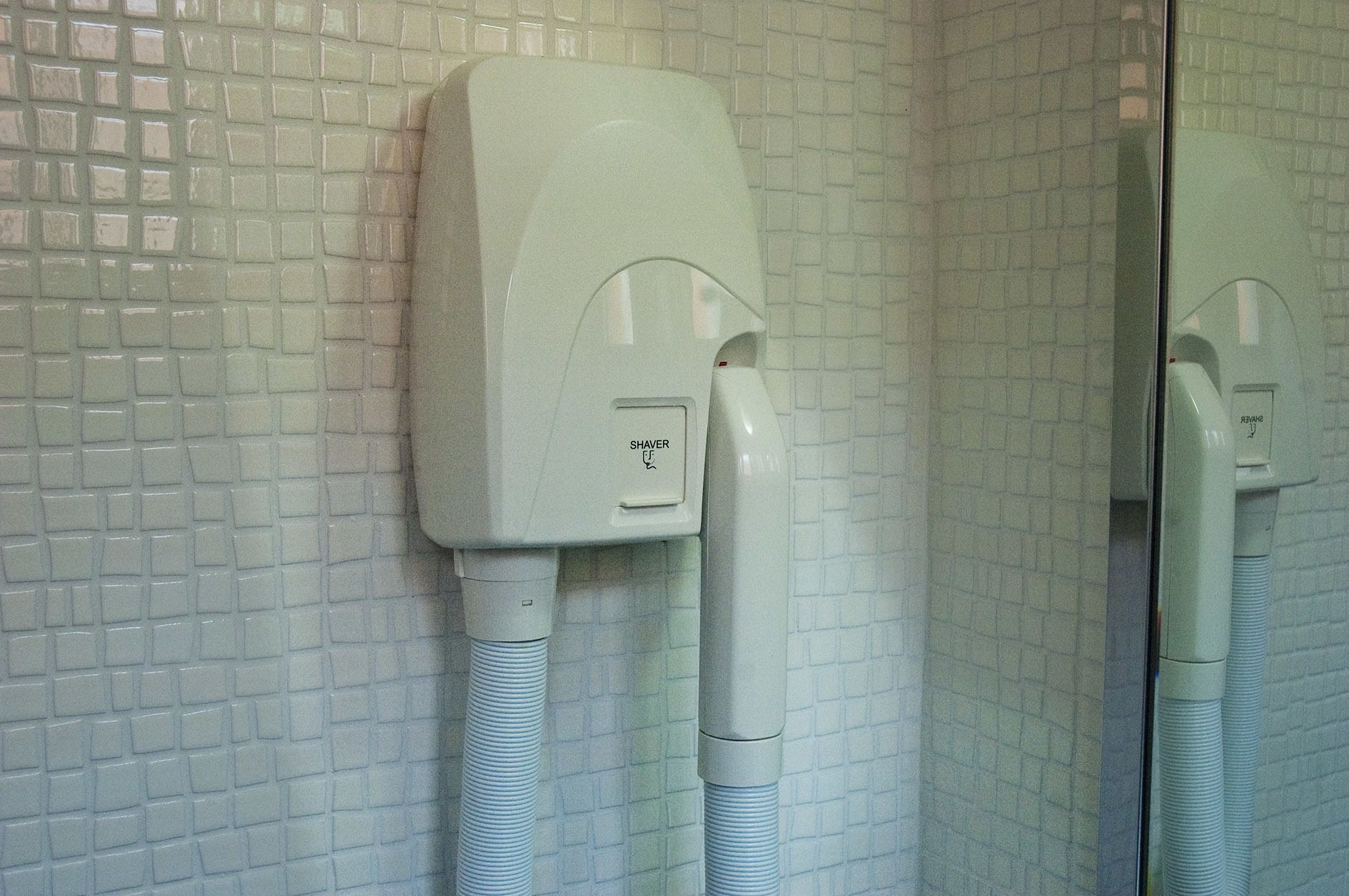 A bathroom with a tiled wall and a mirror reflecting the room.