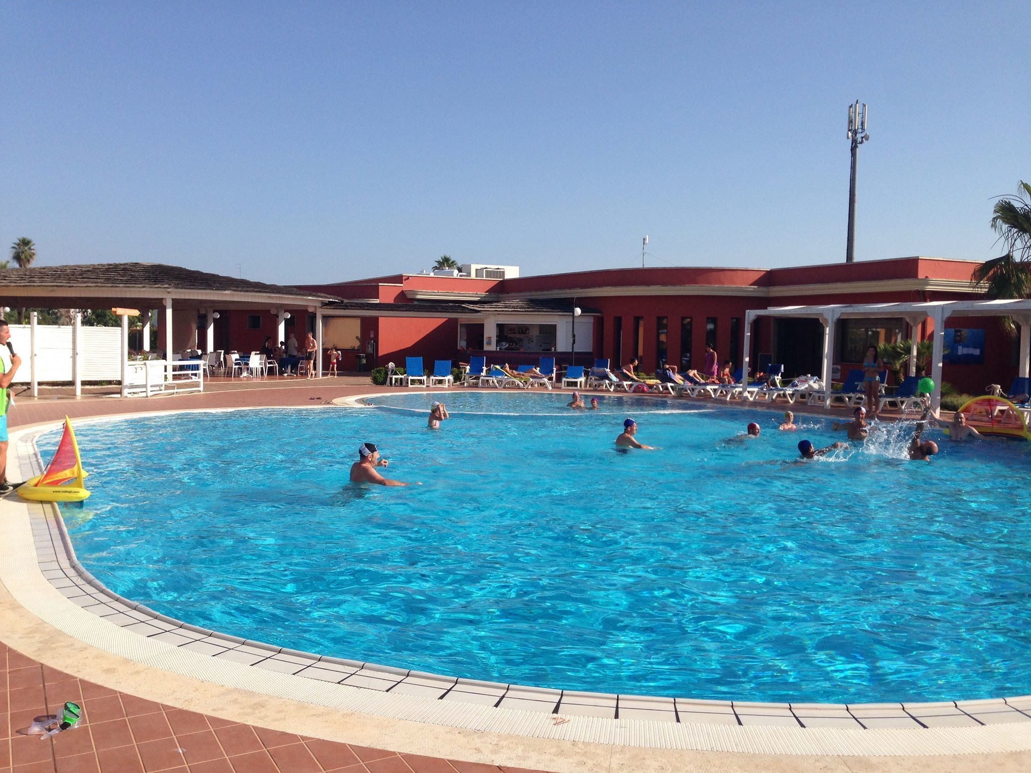 Une piscine dotée de plusieurs couloirs, de chaises longues et d’un espace abrité avec un toit rouge.