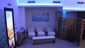 A spa room with a massage table, two massage chairs, a wooden bench, and a wall-mounted artwork. - Baiamalva Resort (Porto Cesareo)