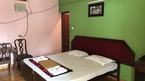 A bedroom with a bed, a desk, and an air conditioning unit. - Indraprastham Tourist Home (Kottayam)