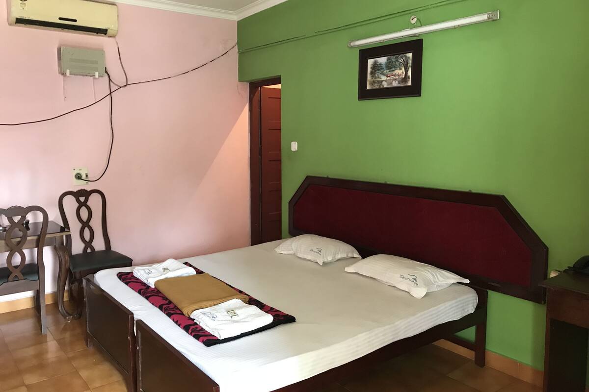 A bedroom with a bed, a desk, and an air conditioning unit.