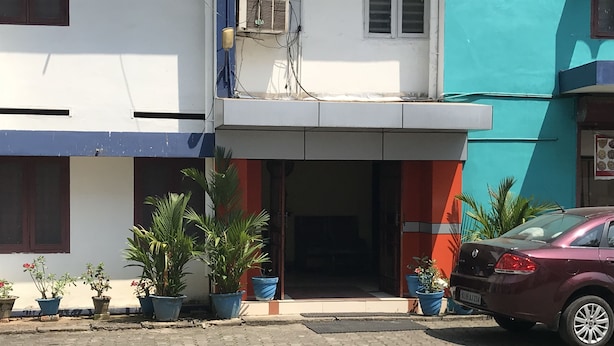 A building with a tiled entrance, potted plants, and a parked car. - Indraprastham Tourist Home (Kottayam)