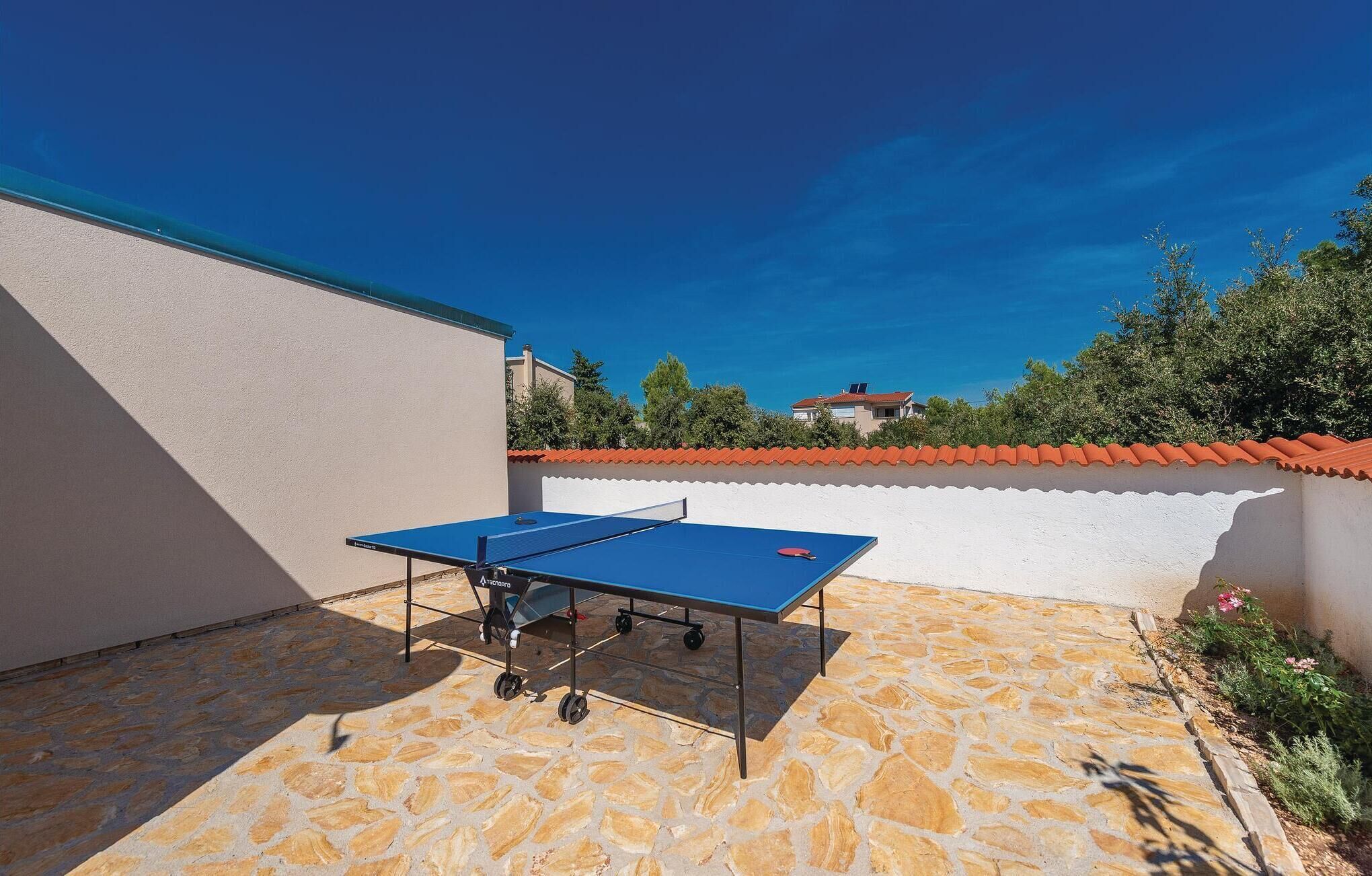 A ping pong table in a courtyard with stone flooring and a white wall.