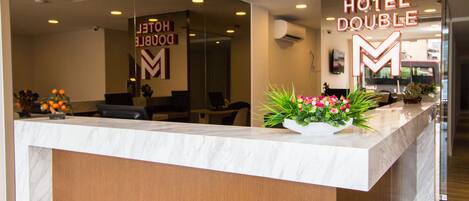 A hotel reception desk with a marble counter, a large 'HOTEL DOUBLE' sign, and a reception area with chairs and a potted plant.