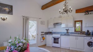 A modern kitchen with white cabinets, a built-in oven, a washing machine, and a dining area with a table set for two. - SPACIOUS 3 ROOMS APT IN LARGE GARDEN HOUSE, WIFFI, CLASS 3 *, 1km from the beach  (le lavandou)