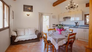 A cozy dining area with a table set for four, wooden chairs, a chandelier, and a view of the kitchen in the background. - SPACIOUS 3 ROOMS APT IN LARGE GARDEN HOUSE, WIFFI, CLASS 3 *, 1km from the beach  (le lavandou)