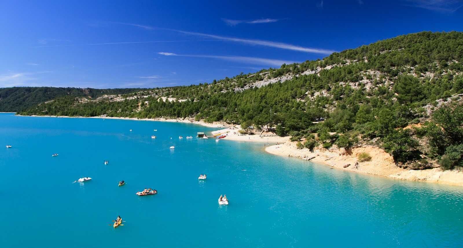 Un paysage côtier avec une eau turquoise cristalline, des bateaux et une colline boisée.