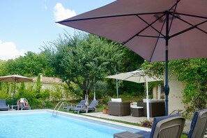 En swimmingpool med liggestole og parasoller, omgivet af grønt.