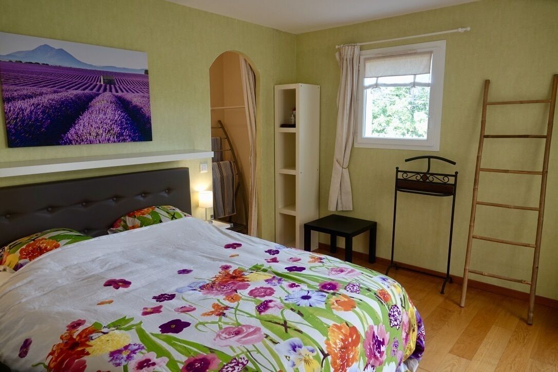 Une chambre à coucher avec une couvre-lit à motifs floraux, une armoire, une fenêtre avec des rideaux et une échelle appuyée contre le mur.