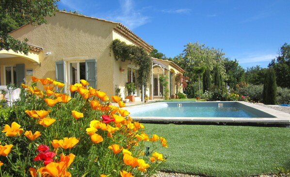 Et hus med swimmingpool, omgivet af en have med gule og røde blomster.