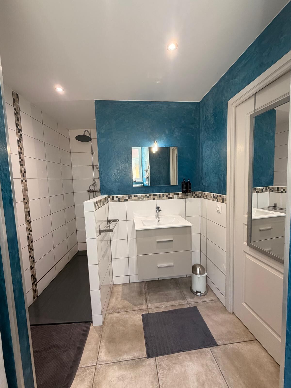 Een badkamer met douche, wastafel, spiegel en betegelde vloer.