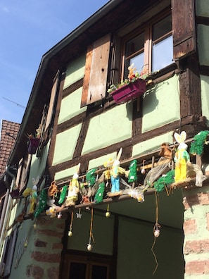 Um edifício tradicional em estilo de enxaimel com uma varanda decorada com figuras temáticas de Páscoa e enfeites pendurados.
