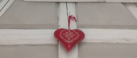 A white air conditioning unit mounted on a white wall with a red heart-shaped decoration hanging below it.