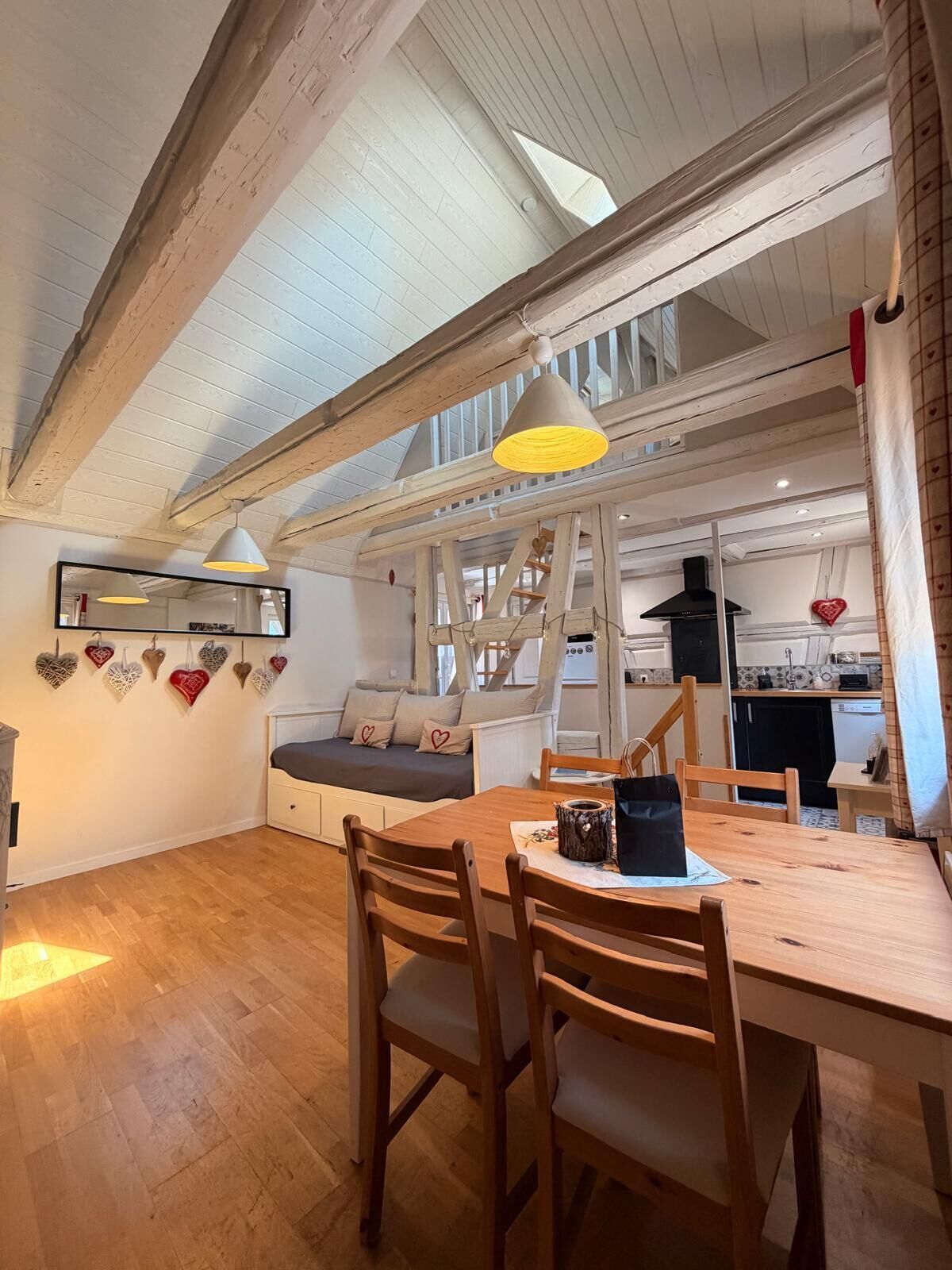 A cozy room with a wooden dining table, chairs, a sofa, and a kitchen area with a stove and cabinets.