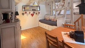 Une pièce chaleureuse avec un plafond en bois, une table à manger, un canapé agrémenté de coussins en forme de cœur et un buffet.