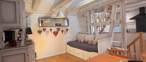A cozy room with a wooden ceiling, a dining table, a sofa with heart-shaped cushions, and a cabinet.
