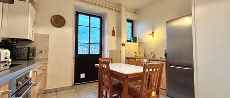 A compact kitchen with a dining table, chairs, a refrigerator, and a window with a view.