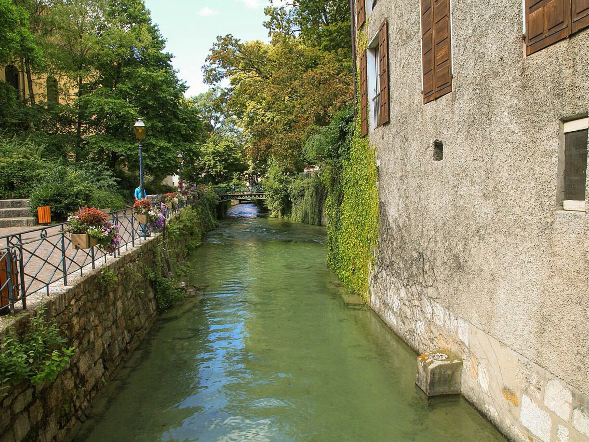 Un canal étroit bordé de murs de pierre et un bâtiment aux volets en bois.