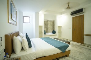 A bedroom with a bed, a window with curtains, a wooden wardrobe, and an air conditioning unit. - Banjara Heritage (Udaipur)