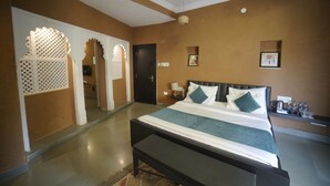A hotel room with a large bed, a bench, a nightstand, and a wall-mounted shelf with bottles. - Banjara Heritage (Udaipur)
