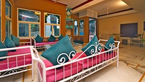 A hotel room with a large bed, multiple windows, and a ceiling fan. - Banjara Heritage (Udaipur)
