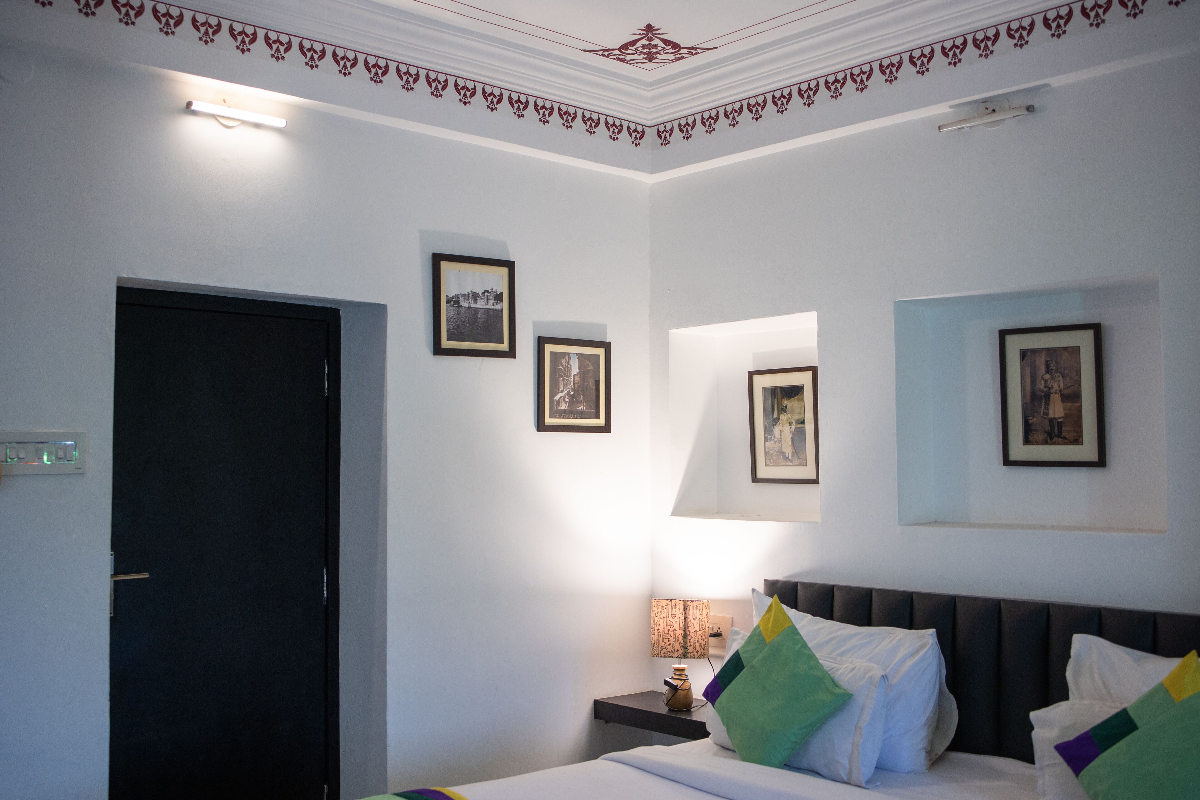 Una habitación de hotel con cama, mesita de noche, lámpara y cuadros en la pared.