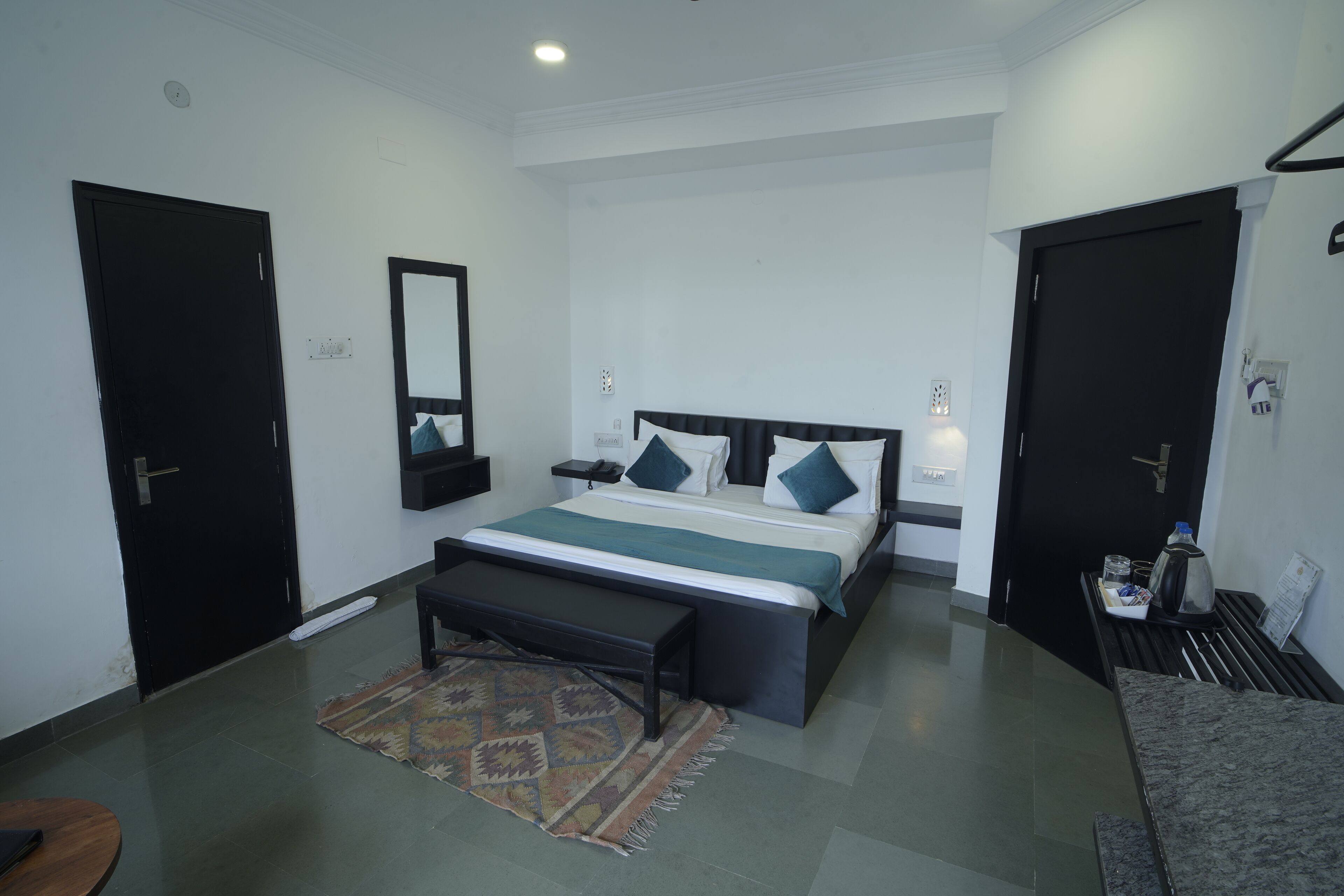 A modern bedroom with a large bed, bedside tables, a bench, and a small table with a kettle.