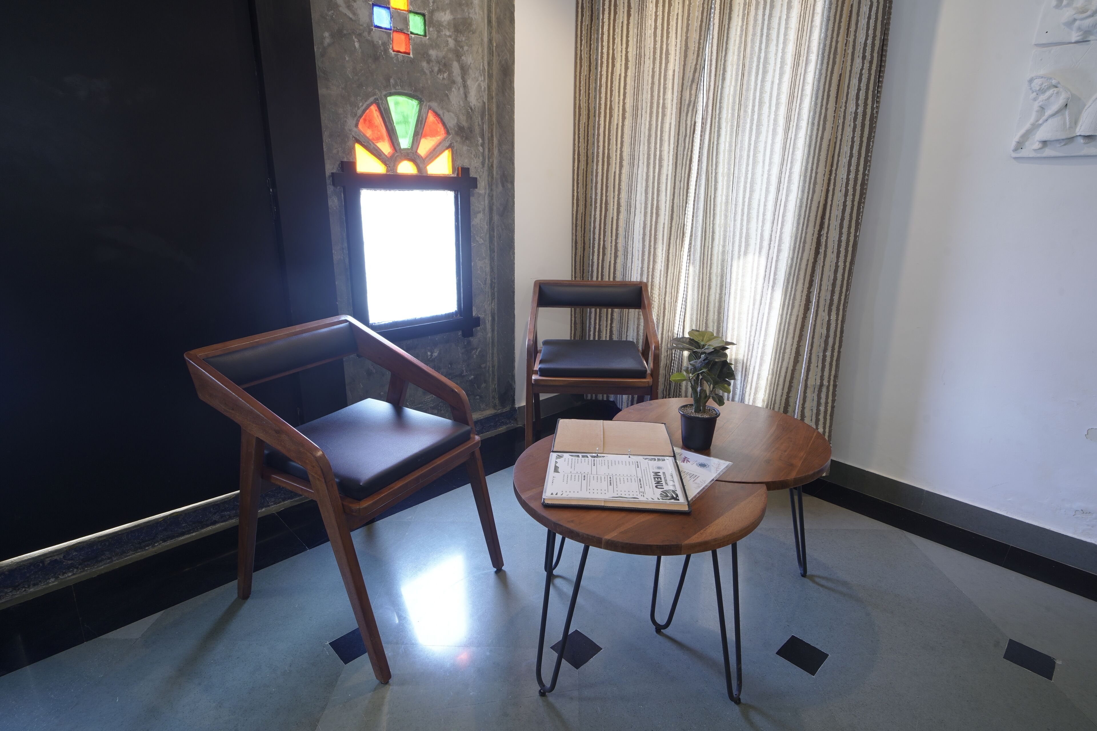 A room with a wooden chair, a table with a menu, a potted plant, and a window with curtains.