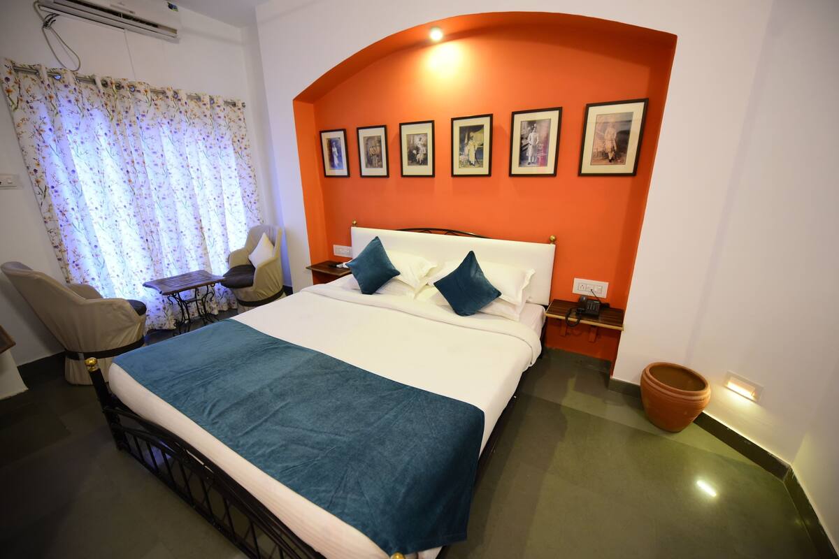 Habitación de hotel con cama, escritorio, una silla, una planta en maceta y un cuadro con fotografías en la pared.