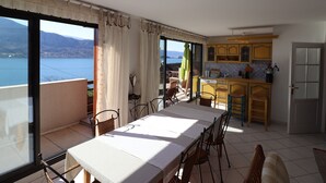 Un coin repas avec une table et des chaises, une cuisine avec des meubles jaunes et une vue sur un lac, visible à travers de grandes fenêtres.